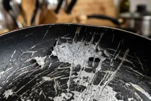 Chảo Chống Dính Bị Trầy Có Dùng Được Không? 3 Dấu Hiệu Nên Tránh 1 Cận cảnh bề mặt chảo chống dính Teflon bị trầy xước nặng, bong tróc lớp phủ đen và lộ lõi nhôm bạc.